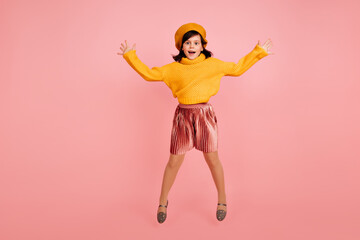 Fototapeta na wymiar Studio shot of good-humoured kid jumping on pink background. Little girl fooling around during shooting.