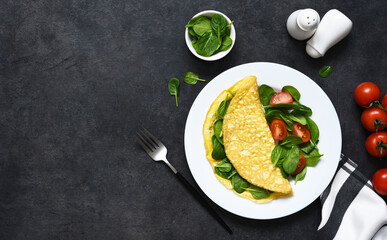Omelet with spinach for breakfast in a plate on a concrete black background. Top view with space for text.