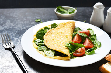 Omelet with spinach and tomatoes for breakfast in a plate on a concrete black background. Good morning.