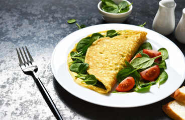 Omelet with spinach and tomatoes for breakfast in a plate on a concrete black background. Good morning.