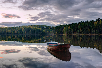 Idyllic landscape of lake surrounded by beautiful autumn pines and trees. Lonely boat in the middle of lake
