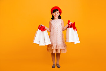 Little french girl holding paper shopping bags. Studio shot of female kid in dress and red beret.