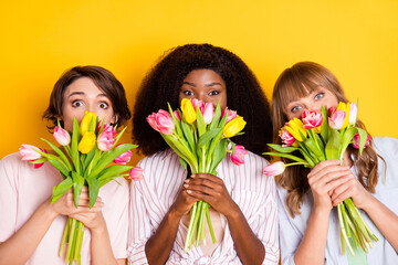 Portrait of three pretty persons hands hold fresh flowers covering mouth isolated on yellow color background