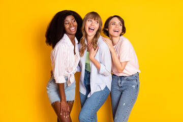 Portrait of three attractive impressed amazed cheerful girls having fun embracing good news isolated over bright yellow color background