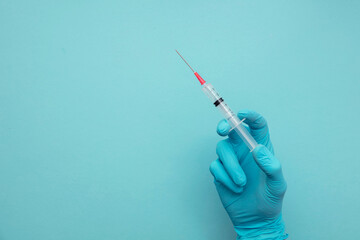 A doctor or nurse wearing blue surgical gloves holding a vaccine syringe