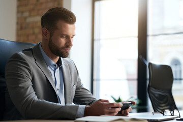 Calm attractive businessman with gadget at his workplace