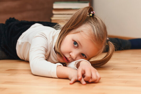 Bored Child lying on the floor. The little girl is tired of home schooling. Tired child at home on background of books