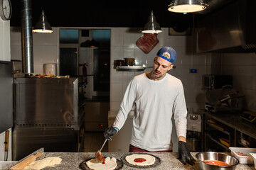 pizza man adds tomato to a pizza in a pizzeria restaurant kitchen