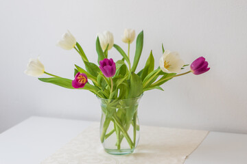 Bouquet of white and pink tulips in a vase on a white table. The background is white.