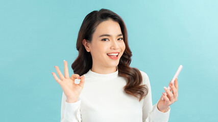 Fototapeta premium Attractive young girl showing ok gesture while holding mobile phone isolated over white background