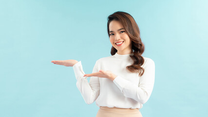 Portrait of Asian beautiful young girl raising both hands aside show something, isolated in blue background.