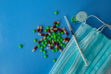 Various tablets and capsules, syringe, protective masks, on a blue background