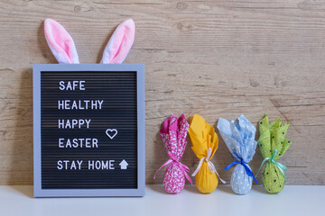 Decorative sign with rabbit ears and colored eggs in side with the easter message: Safe, healthy, happy easter, stay home.