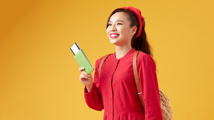 Portrait of a cheerful cute asian girl traveller showing passport with tickets isolated over yellow background