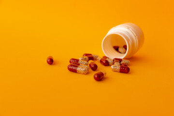 red and white capsules and a white jar of capsules lie on the table on a yellow background close up