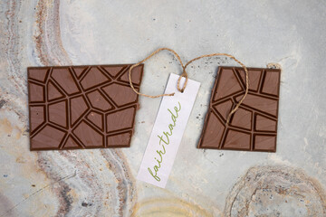 chocolate bar lies on light stone background with a small label that says fair trade and a vintage string