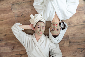 Two young beautiful girlfriends are smiling and uses cosmetic facial mask. Healthy beauty clean treatment and cosmetology products concept
