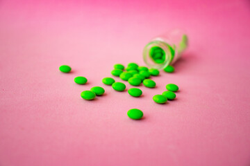 a glass ampoule is lying on the table a pile of green pills close up on a pink background