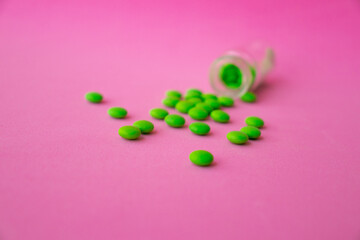 a glass ampoule is lying on the table a pile of green pills close up on a pink background
