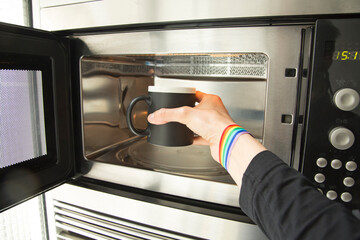 Hand with rainbow bracelet putting a black bowl in the microwave