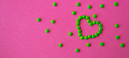 heart of green pills on a pink background, heart-shaped pills laid out on a table close-up