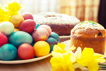 Easter orthodox sweet bread, kulich, colored eggs and a bouquet of daffodils.
