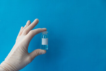 a hand in a white protective medical glove holds the vials of the vaccine close up on a blue background