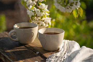 Coffee with milk, cocoa, tea in cups with heart decor, lace napkin on a wooden table. Cherry blossoming branches, spring mood. Outdoor, brunch, refreshments