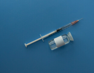 a syringe with a vaccine and ampoules with a vaccine against infections close-up on a blue...