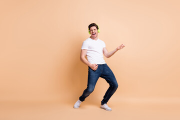Fototapeta na wymiar Full size photo of optimistic brunet man dance play guitar wear white t-shirt jeans isolated on beige color background