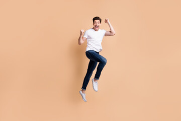 Fototapeta na wymiar Full size profile photo of hooray brunet man jump wear t-shirt jeans sneakers isolated on beige background