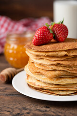 Stack of thin french crepes served with strawberries and honey. Rustic style