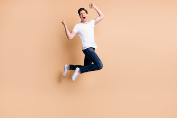 Fototapeta na wymiar Full size profile photo of hooray brunet man jump yell wear t-shirt jeans sneakers isolated on beige color background