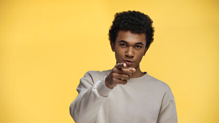 Fototapeta premium curly african american teenage boy pointing with finger isolated on yellow