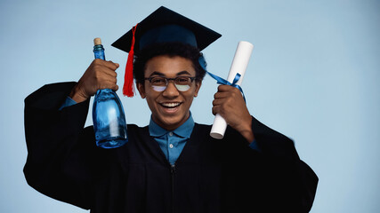 african american teenage boy in graduation gown and cap holding diploma and bottle with champagne...