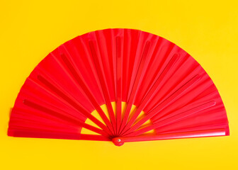 Red hand fan on yellow background, top view