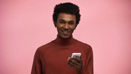smiling african american teenager in turtleneck sweater and glasses looking at camera while holding...