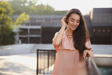 Beautiful young woman in stylish pink dress near railing outdoors