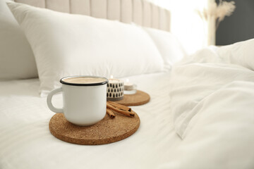 Fototapeta na wymiar Cup of aromatic coffee and cinnamon sticks on bed with soft blanket, closeup. Space for text