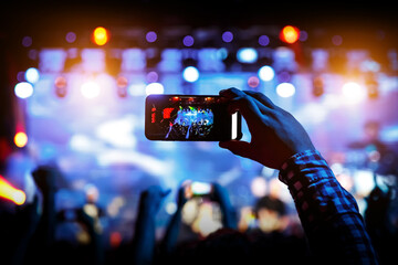 Hand with the smartphone turned on to record or take pictures during the live concert.