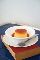 Homemade Caramel custard pudding in a plate on a red book placed on a blue table.