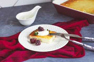 Cottage cheese casserole on a white plate and tea in a burgundy cup on a gray background