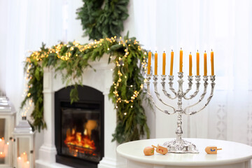 Silver menorah near dreidels with symbols He, Pe, Nun, Gimel on white table in room, space for text