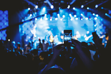 Hand with the smartphone turned on to record or take pictures during the live concert.