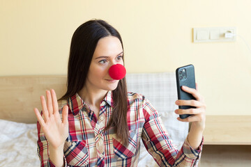  A girl with a red clown nose fools around in front of the phone, takes a selfie, congratulates friends on April Fools' Day