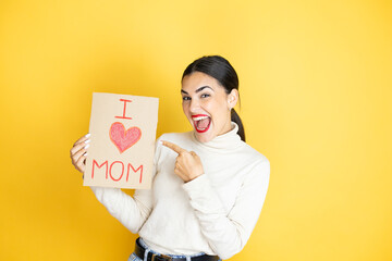 Beautiful woman celebrating mothers day holding poster love mom message amazed and pointing with hand and finger