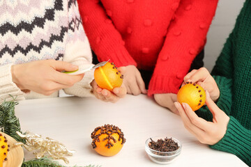 Obraz na płótnie Canvas Friends decorating fresh tangerines with cloves at light wooden table, closeup. Making Christmas pomander balls