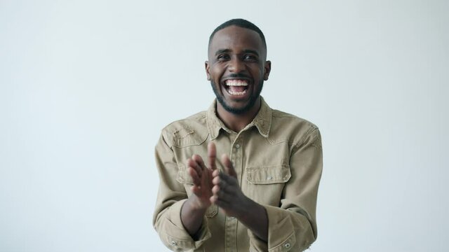 Slow motion portrait of joyful African American man clapping hands with crazy facial expression looking at camera on white background. People and ovation concept.