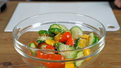 Close up fresh vegetables salad dish with cucumbers red cherry tomatoes yellow bell peppers sprinkled with sesame seeds in glass bowl, healthy eating food dieting and vegetarian concept