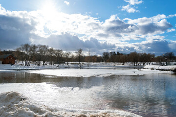 Winter landscape with bright sun in blue sky. Ice pond. The beginning of spring